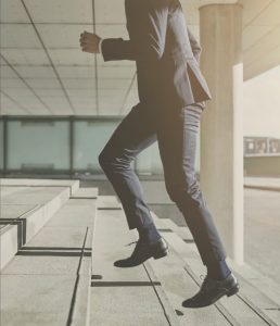Business professional in a suit stepping up concrete stairs, symbolizing progress and elevation.